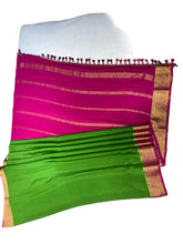 A folded and draped saree laid flat on a white sheet, featuring a bright magenta pink body with gold zari stripes, a green pallu section with gold border, and a pink tassel border.